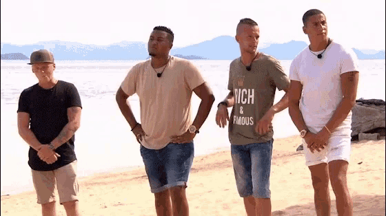 four men standing on a beach with one wearing a shirt that says abercrombie & fitch & famous