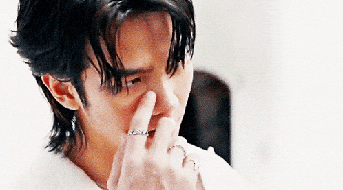 a close up of a man covering his nose with his finger .