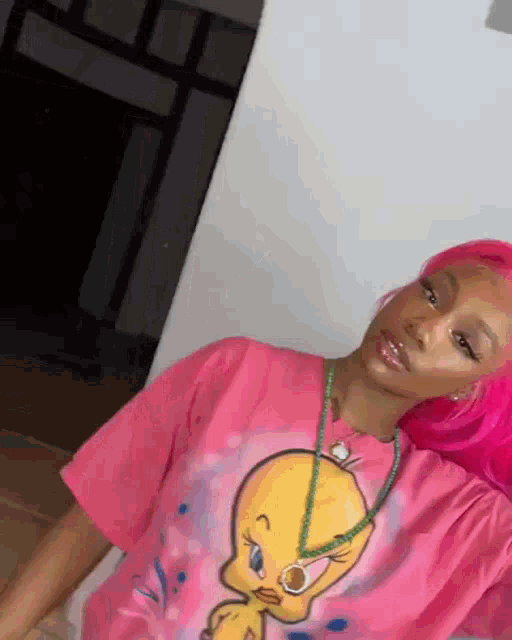 a woman with pink hair is wearing a pink t-shirt with tweety on it and a necklace .