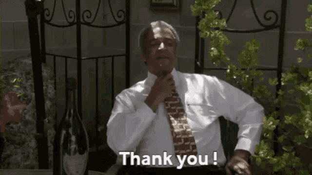 a man in a white shirt and tie is sitting in front of a bottle of champagne and says thank you !
