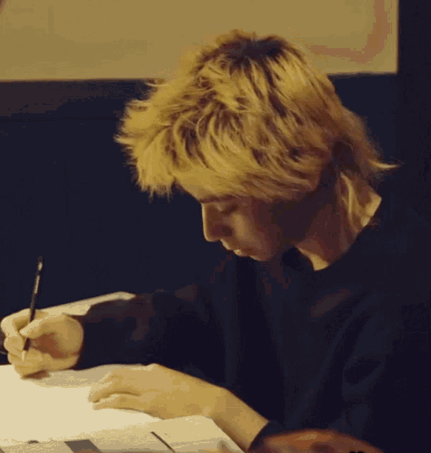 a young man with blonde hair is writing on a piece of paper