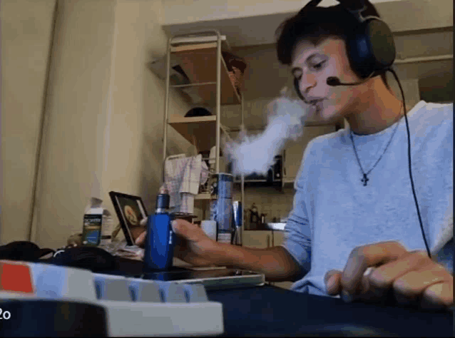 a man wearing headphones is smoking an electronic cigarette while using a keyboard