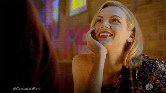 a woman is smiling while sitting at a table with a bottle of beer and #chicagofire written on the bottom