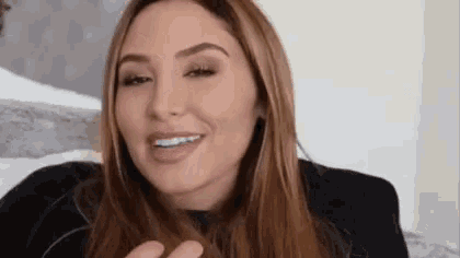 a woman with long brown hair is smiling and holding her hair in her hand .