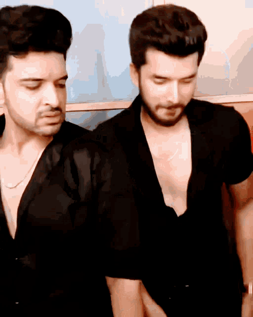 two men wearing black shirts are standing next to each other with their eyes closed