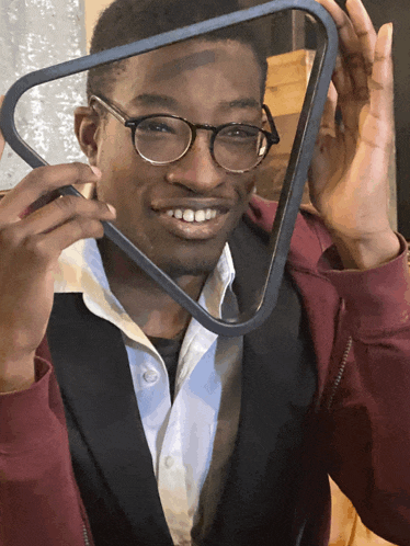 a man with glasses and a red jacket holds a triangle in front of his face
