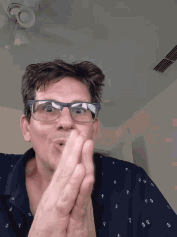 a man wearing glasses is covering his mouth with his hand