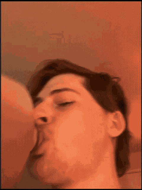 a man with a beard is drinking from a bottle with his eyes closed