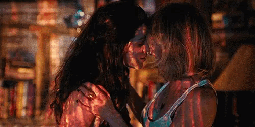 two women are kissing in a dark room with a projector projected on their bodies .