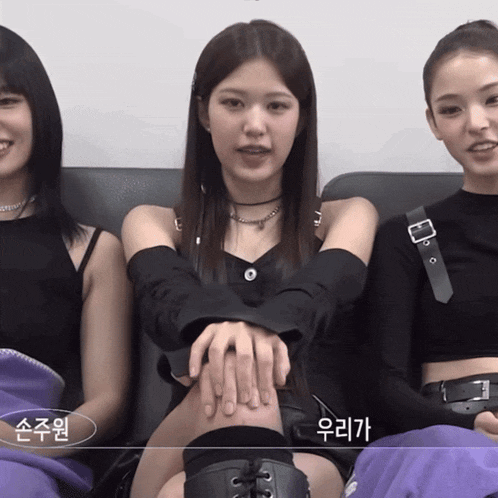 three girls are sitting on a couch with their hands on their knees and one of them is wearing a purple blanket