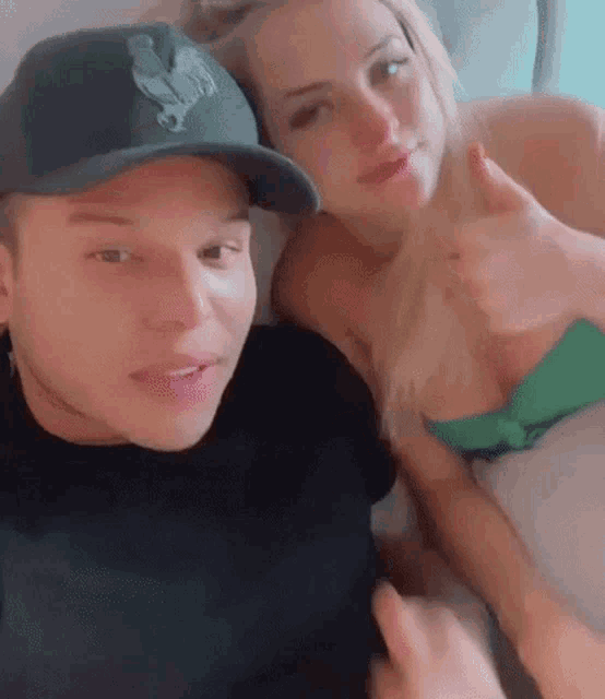 a man and a woman are sitting next to each other on a bed and the woman is giving the man a thumbs up .