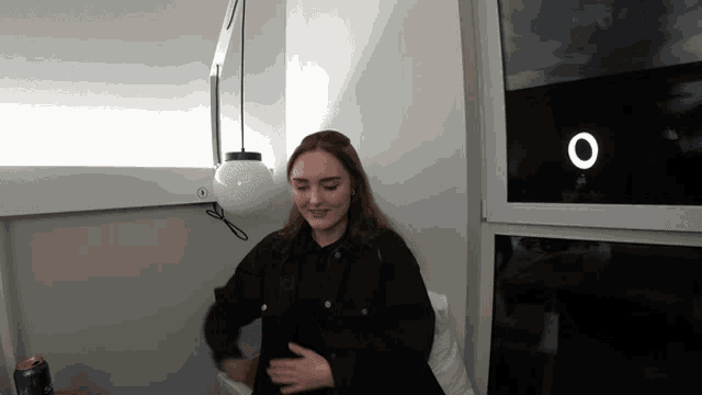 a woman in a black shirt is sitting in front of a window with an o on it