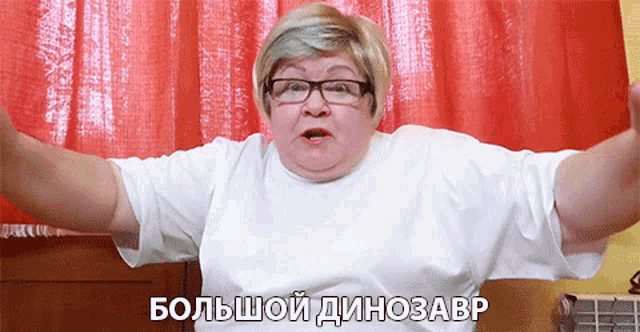 a woman wearing glasses and a white shirt is standing in front of a red curtain and says большой динозавр