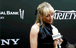 a woman is holding a microphone in front of a variety sign