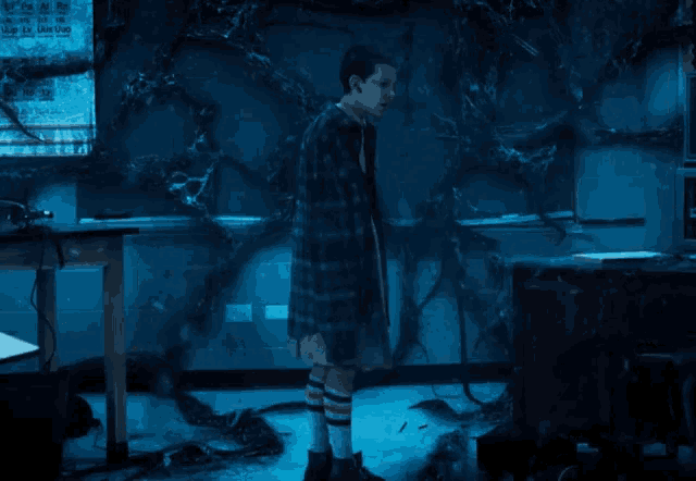a girl in a plaid coat and striped socks is standing in a dark room