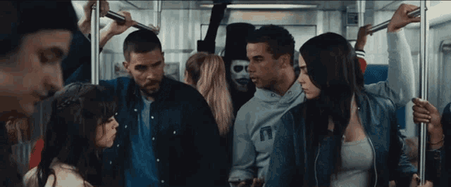 a man in a mask is standing in the middle of a crowd of people on a train