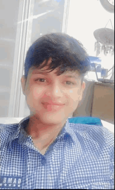 a young man in a blue and white checkered shirt is taking a selfie .