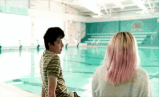 a boy and a girl sit in front of a swimming pool with a sign that says dolphins on it