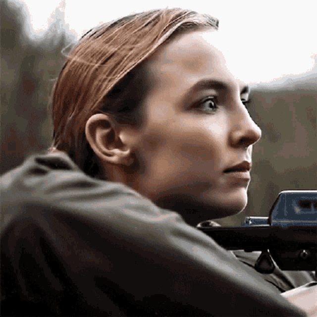 a woman in a green jacket is holding a gun .