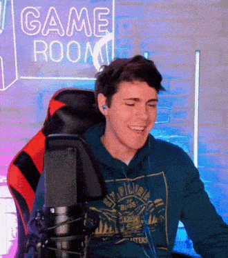 a man sitting in front of a microphone with a game room sign in the background