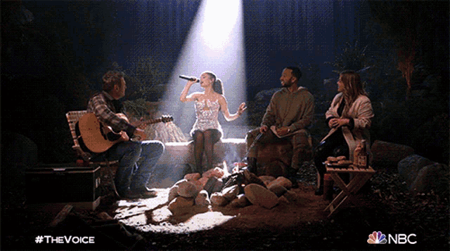 a group of people are sitting around a campfire and a woman is singing