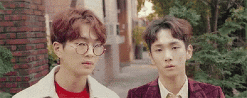 two young men are standing next to each other on a sidewalk . one of the men is wearing glasses .