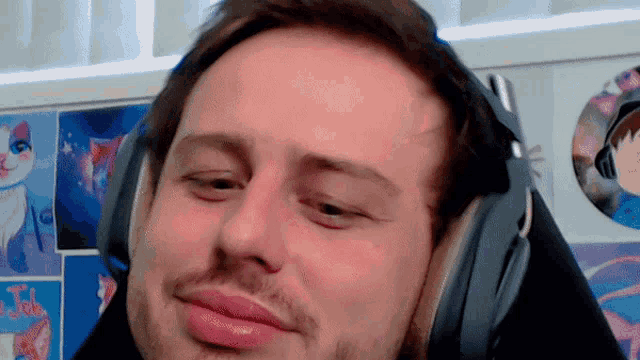 a man wearing headphones looks at the camera with a cat on the wall in the background