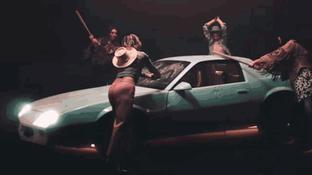a group of people standing around a car with one wearing a hat
