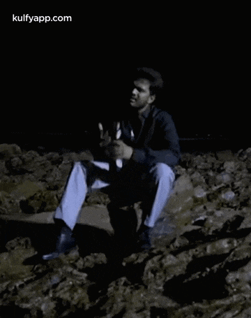 a man is sitting on a rock in the dark holding a bottle of water .