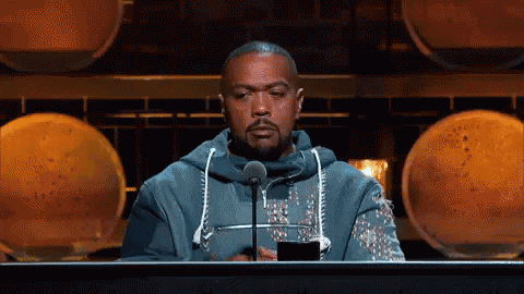 a man in a blue hoodie stands in front of a microphone with his eyes closed