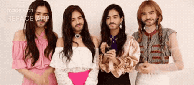 a group of men with long hair and beard are standing next to each other in front of a white wall .
