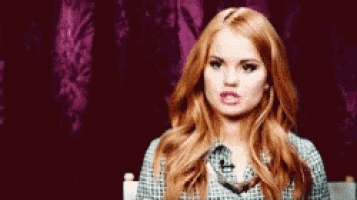 a woman with red hair is making a funny face while sitting in front of a purple curtain .