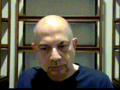 a bald man with a beard wearing a blue shirt looks at the camera