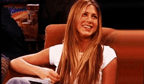 a woman with long blonde hair is sitting on a couch and smiling
