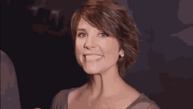 a woman with short hair is smiling and holding her fist in the air