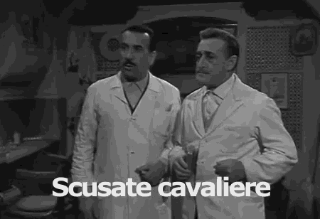 two men in white coats are standing next to each other in a room and the words scusate cavaliere are on the screen .