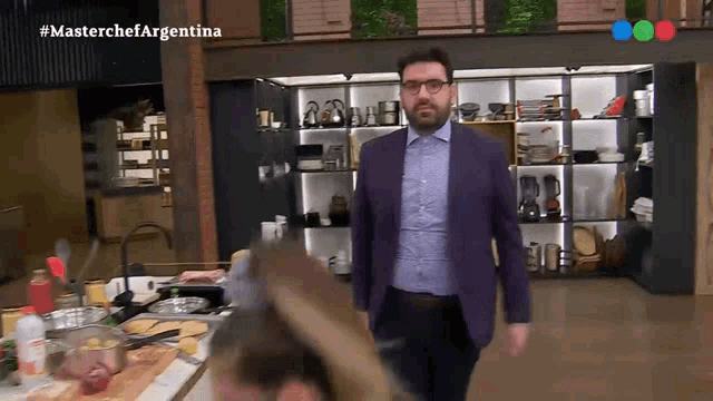 a man in a purple suit is walking in a kitchen with the hashtag #masterchefargentina on the bottom