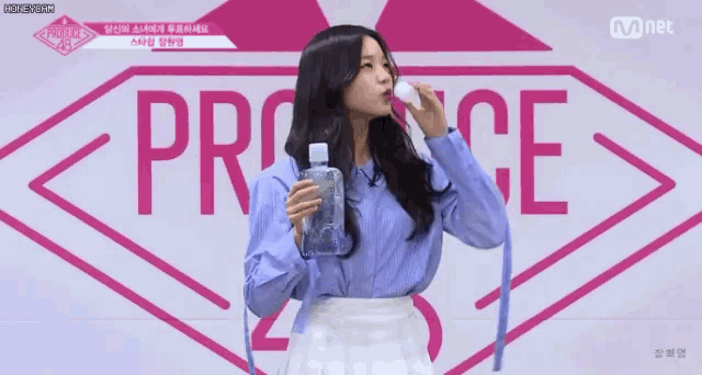 a girl is drinking water from a bottle in front of a mnet logo .