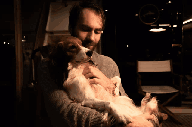 a man is holding a dog in his arms with a chair in the background