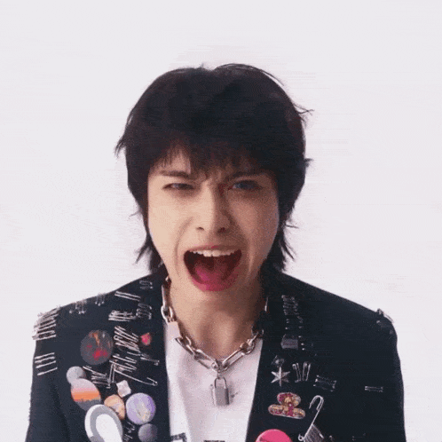 a man wearing a jacket with pins and a necklace that says tribe on it