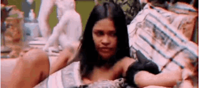 a woman is laying on a bed with a statue in the background and looking at the camera .