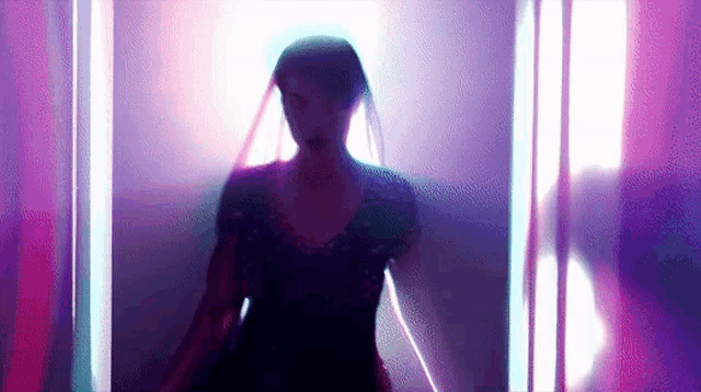 a woman in a purple dress is standing in a room with purple lights behind her .