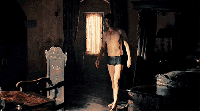 a man without a shirt is standing in a dark room in front of a window