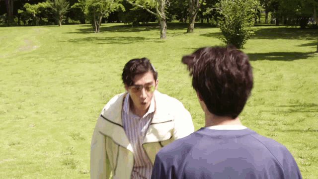 two men are standing in a grassy field talking