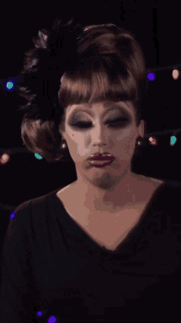 a drag queen wearing a black dress and a black feather in her hair