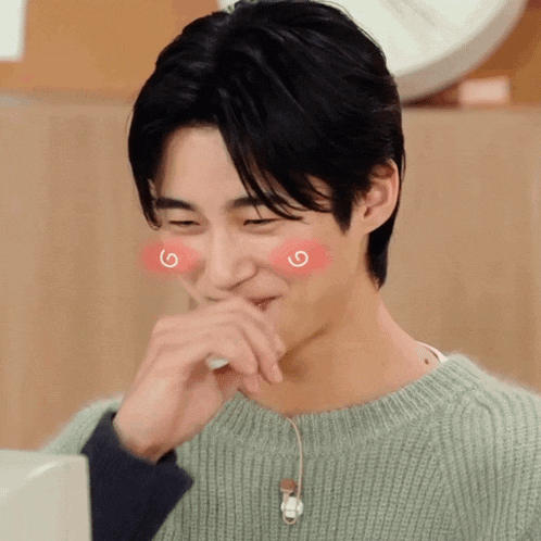 a young man wearing a green sweater is covering his mouth with his hand