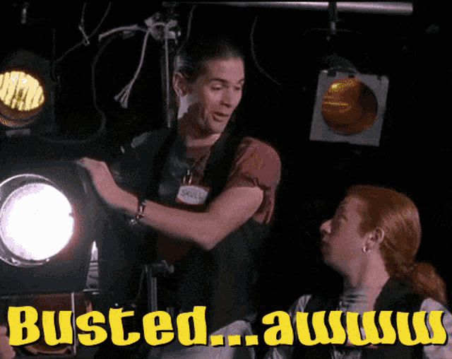 a man and a woman are standing in front of a spotlight with the words busted awww written on the bottom
