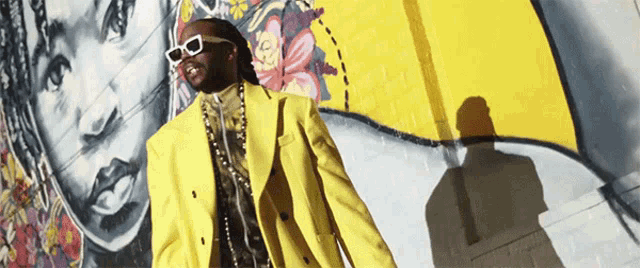 a man wearing sunglasses and a yellow suit stands in front of a mural