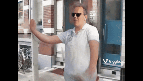 a man wearing sunglasses is standing in front of a building with the number 27 on the door