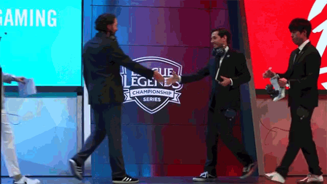a man shakes hands with another man in front of a league of legends championship series sign